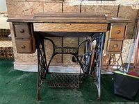 Front view of antique Singer treadle sewing machine with ornate treadle base and wooden cabinet with drawers.