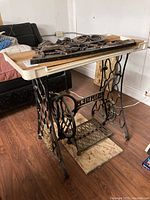 Side view of Singer sewing table stand with plastic wall decor on top, showing cast iron intricate legs and the tabletop.