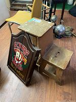 Photo showing worn wooden step stool and dart board with pub sign design leaning against it
