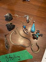 Photo taken showing all sterling silver jewelry pieces including necklace, earrings, pendants, bracelet, and brooch arranged on a wooden surface with a green tape labelled 'Sterling'.