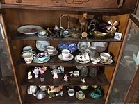 Tea cups, saucers, figurines, plates, metal ware and glass items arranged in cabinet shelves