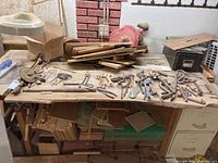 Wide view of vintage and antique hand tools arranged on a rustic wooden board with wood pieces underneath and nearby.