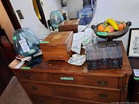 Top-down view of the dresser top with wood jewelry boxes, glass vase, ceramic bowl with faux fruit, and other decorative items.