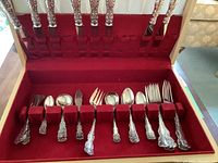 Open wood box showing red velvet interior with eight stainless steel–stem knives upright and row of sterling flatware pieces