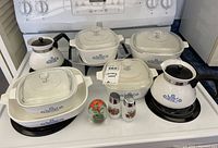 Full set of Corning Ware cookware with coffee pots, salt and pepper shakers, paper weight, and chafing stand arranged on stove
