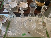 Overview of all glassware items including four decanters with stoppers, a lidded dish, and multiple shot glasses arranged on a table.