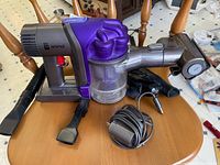 Full shot of Dyson DC34 Animal cordless vacuum with crevice and brush attachments and charger on chair.