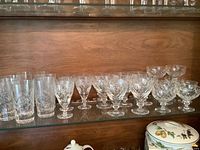 Full view of all glasses showing tumblers, small wine glasses, medium wine glasses, and dessert glasses arranged on wood shelving.