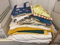 Stack of assorted vintage linens showing various colors, textiles, and lace edges