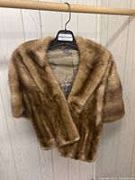 Full view of the vintage mink shawl hanging on a black hanger, showing the soft light brown fur and overall size and shape.