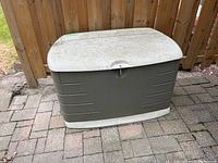 Rubbermaid patio storage box, showing weathered and locked lid on greenish-gray base with off-white lid.