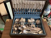 Open wooden cutlery box with upper knife slot and piled flatware below