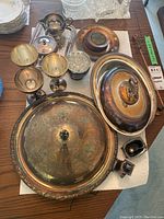 Overview of all silver plated serving dishes and tableware items arranged on table, showing tarnish wear and ornate decorative details