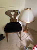 Photo showing MCM Anthes Baetz wooden framed chair with black upholstered seat next to a twisted rope-style brass table lamp with white and gold-trimmed lampshade.