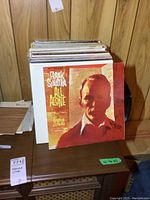 Photo of vinyl record albums with Frank Sinatra's 'All Alone' album cover prominently visible, showing the collection in a wood-paneled room.