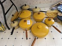 Overview of 7 yellow West Bend cookware pieces on floor, including pots and sauté pan with lids, wooden handles and knobs visible.