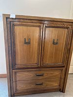 Front view of wooden armoire showing two doors with metal handles and two drawers below.