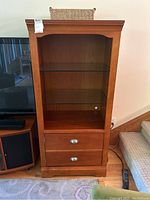 Front view of wood cabinet showing two glass shelves and two drawers with metal handles.