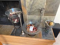 Photo of two glass potpourri bowls with metal stands and dried decorative elements in front of a fireplace.