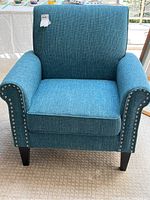 Front view of blue upholstered armchair with fixed cushion and dark wooden legs, and nailhead trim along arms.