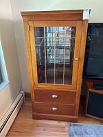 Full frontal view of the wooden display cabinet with glass door and two lower drawers, showing the medium brown finish and decorative glass grid in the door.