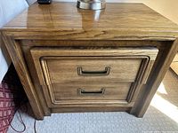 Front view of one wooden end table showing two drawers with metal handles and wood grain finish.