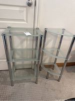 Photo of two glass shelves; one rectangular with three glass shelves and chrome supports, the other a corner shelf with three curved glass shelves and chrome supports.