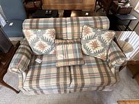 Front view of the plaid patterned love seat with three cushions including two floral patterned and one plaid cushion.