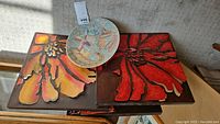 Photo showing the 3 metal wall art pieces with warm floral design and the decorative wall plate placed together on a surface.