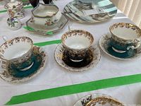 Three Royal Albert teacups and saucers from the Regal series with teal and gold floral design, displayed on a white cloth.