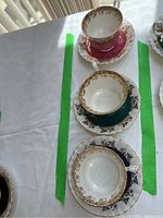 Above view of the three Royal Albert teacup and saucer pairs lined up on a table showing the intricate gold floral trim and scalloped edges on pink, teal, and blue bases.