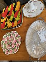 Top view showing colorful ceramic platters with chili peppers, floral rose design platters, and glass divided serving tray with metal handles.