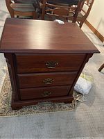 Front view of the wood side table showing three drawers with brass handles and base design