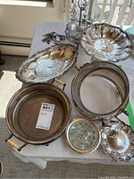 Top-down photo showing several silver plate trays, metal pot with wooden handles, and additional smaller silver pieces including flower frog and caddies, all showing light to moderate tarnish.