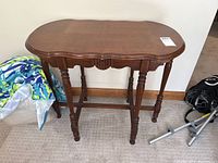 Front angled view of a vintage wooden table showing scalloped edges and turned legs with stretchers.