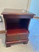 Front view of the wooden side table showing its top, open shelf, drawer, and base.
