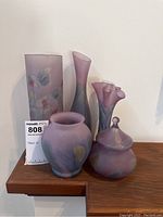 Front view of the 5 colour glass vases with purple, grey, beige tones on wooden shelf
