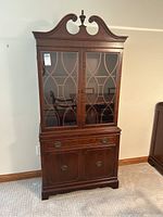 Front view of vintage wooden cabinet with detailed glass doors and carved top.