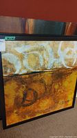 Photo of a square framed abstract painting with warm earthy tones and textural layered design.