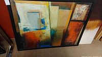 Photo of wood framed abstract painting featuring geometric shapes and multiple colors, loose in frame.
