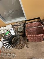 Photo showing assortment of wicker baskets, a candle holder, and the base of a metal plant stand.