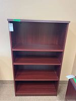 Full front view of the wood bookcase showing four shelf compartments, dark reddish-brown finish.