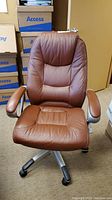 Front view of the brown leather office chair highlighting seat, armrests, and backrest with visible stitching and padding.