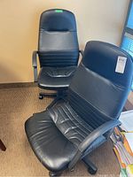 Two black office chairs positioned side by side against a wall, showing overall design and condition