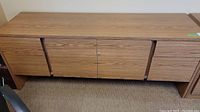 Front view of long woodgrain credenza with 2 cabinet doors in center and 3 drawers on each side, showing overall condition and finish.