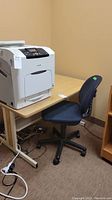 Photo of wood finish desk with metal legs and blue upholstered office chair on wheels, showing front angle with printer on desk.