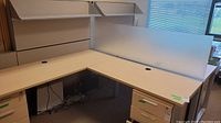 L-shaped cubicle desk with glass divider, showing drawers and cable management holes
