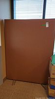 Single brown fabric office divider panel standing upright next to a window, showing full front face.