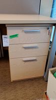 Front view of a wooden filing cabinet showing three drawers with silver horizontal handles, top drawer featuring a lock and key.