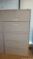 Front view of gray metal filing cabinet with five drawers, top drawer locked.